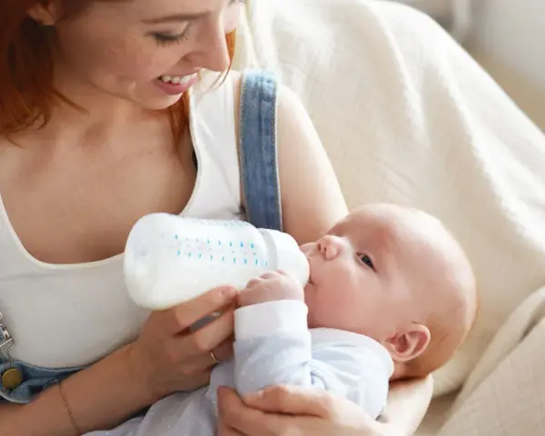 Mamma con capelli rossi nutre il suo neonato con latte artificiale ogni 2 ore. Il piccolo beve con gusto dalla bottiglia.