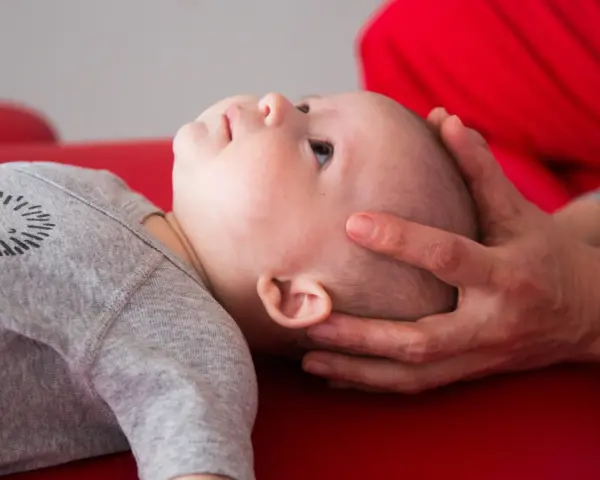 Un neonato sbatte la testa sul petto, con mani adulte che lo sostengono delicatamente.
