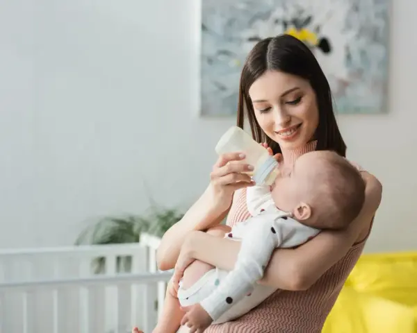 Mamma sorridente nutre il neonato con latte artificiale. Il piccolo potrebbe avere cacca liquida, ma ora è felice.