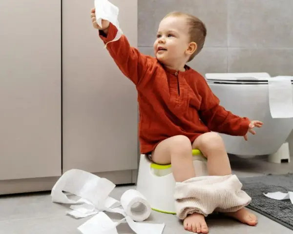 Bambino di 4 anni sul vasino, con rotoli di carta igienica sparsi. Un piccolo disastro, ma un grande passo verso l'indipendenza!