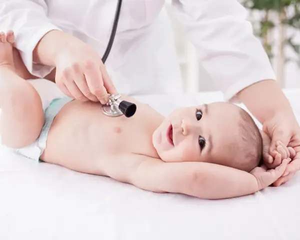 Un neonato sorride mentre il pediatra ascolta il suo respiro con uno stetoscopio.