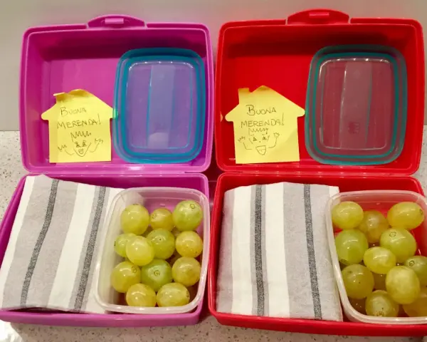 Due lunchbox rosa e rosse pronte per le merende per bambini, con uva e un bigliettino "Buona Merenda!".