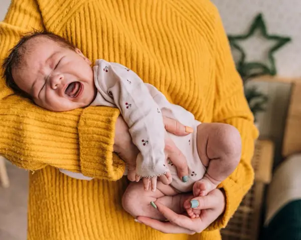 Neonato di 11 mesi con scatti nervosi, piange tra le braccia di chi lo tiene, avvolto in un maglione giallo.