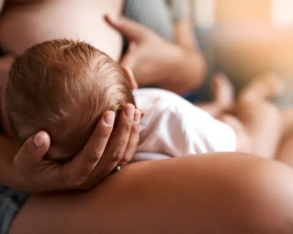 Un neonato si nutre al seno, la sua testolina è tenuta da una mano. La montata lattea non arriva, ma l'amore è presente.