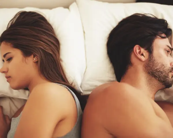 Coppia a letto, schiena contro schiena, con espressioni pensierose. Un'immagine che fa riflettere su come capire se una relazione è finita.