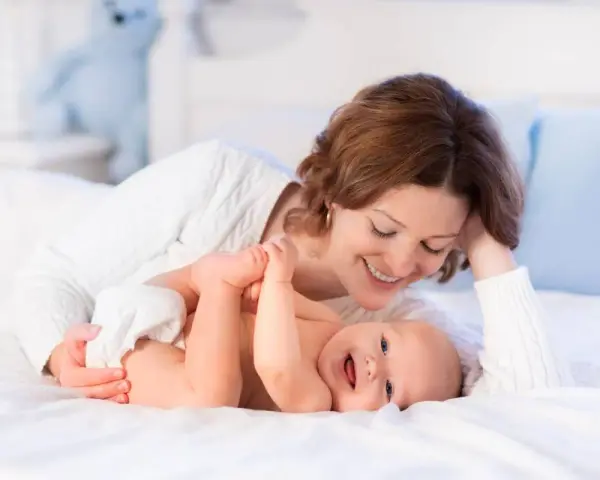 Mamma sorride mentre gioca con il suo neonato, svegliandolo dolcemente per mangiare.