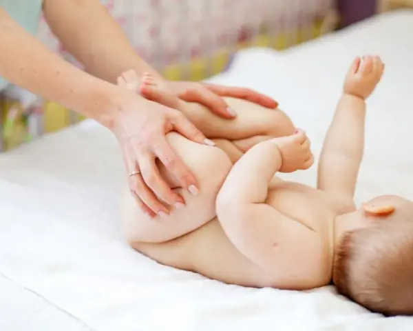 Mani che aiutano il neonato a fare la cacca con movimenti delicati sulle gambine.