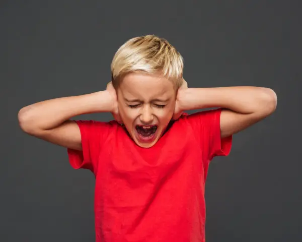 Bambino di 7 anni in crisi di rabbia, urla coprendosi le orecchie.