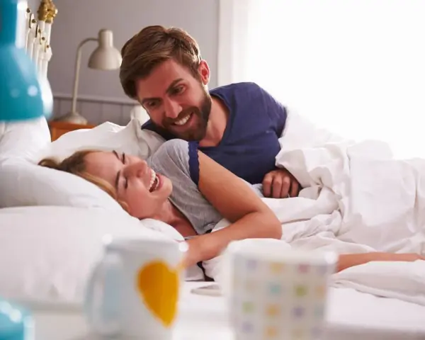 Coppia sorridente a letto, un momento di gioia che va oltre i rapporti promiscui, un legame profondo.