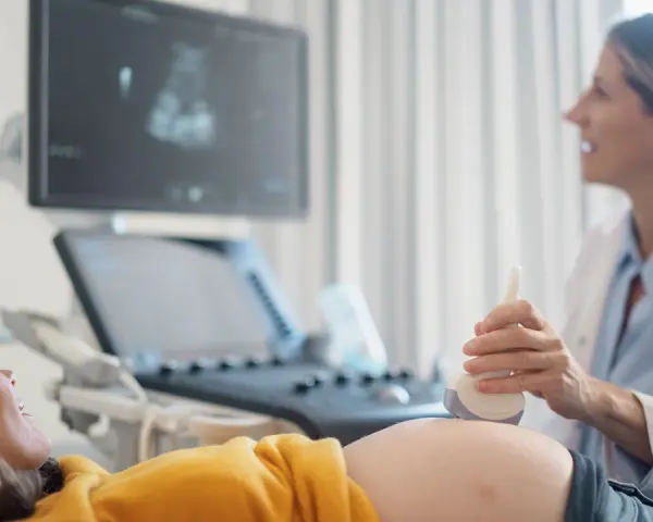 Ecografia di una donna incinta, con il medico che usa la sonda per sentire il battito del feto. L'emozione sul volto della futura mamma è palpabile.