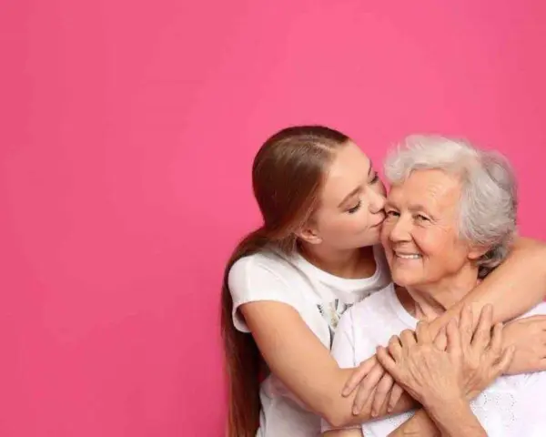 Una ragazza bacia la guancia della nonna, abbracciandola. Si vede che i figli assomigliano ai nonni, un legame d'amore.