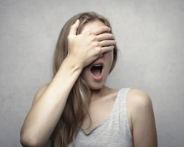 Ragazza con la mano sugli occhi, bocca spalancata, forse per la fobia del vomito (emetofobia).