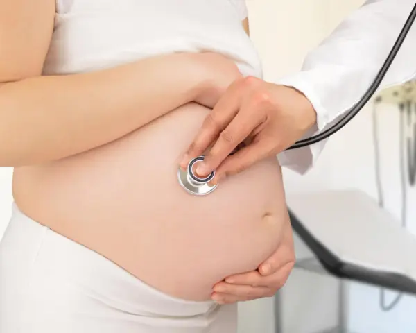 Visita medica per monitorare la gravidanza. Il medico ascolta il battito cardiaco del feto con uno stetoscopio sul pancione.