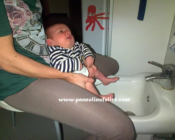 Un bimbo fa pipì in giro mentre è seduto sul lavandino, con un adesivo di polpo sul muro.