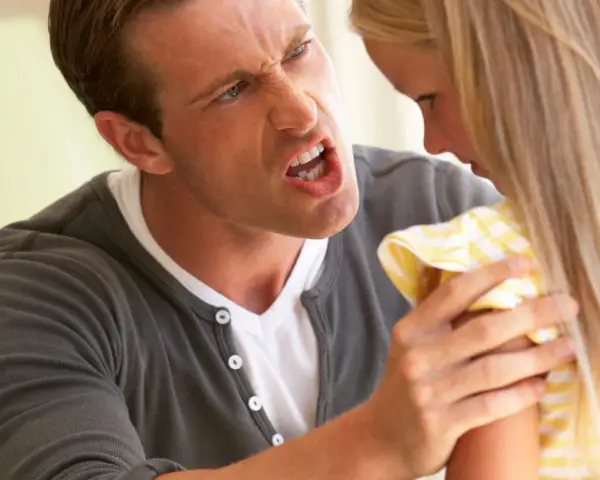 Un uomo arrabbiato urla contro una bambina. La sua espressione facciale è feroce, con gli occhi stretti e la bocca spalancata. La bambina, con i capelli biondi lunghi, sembra spaventata e si ritrae. La scena evoca un senso di tensione e conflitto famil...