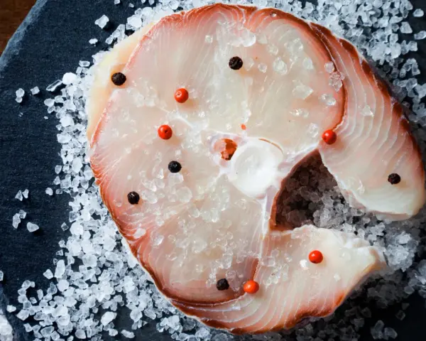 Raw swordfish steak with salt and peppercorns on a dark slate.