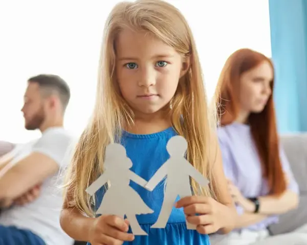Bambina con sagome di carta di una coppia, mentre i genitori separati sono sullo sfondo.