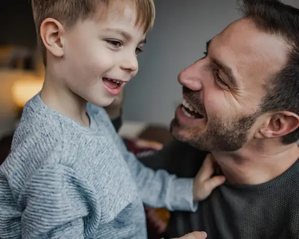 Un padre e suo figlio ridono guardandosi negli occhi. Il bambino, con un maglione grigio, sembra chiedere "perché mio figlio non mi chiama mamma?".