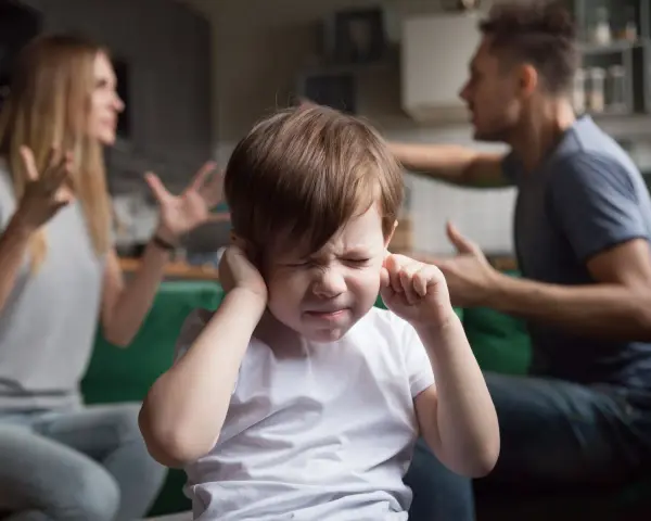 Bambino con le mani sulle orecchie, mentre i genitori litigano. Una scena che mostra una crisi di coppia con figli.