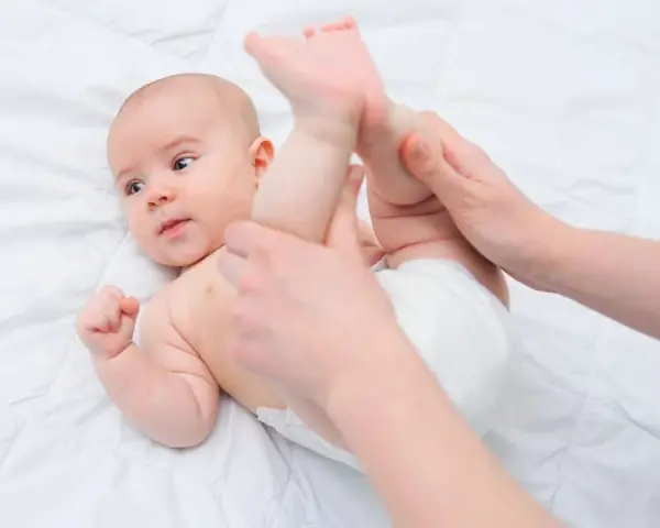 Mani che aiutano un neonato a liberarsi dall'aria nella pancia, con le gambine sollevate delicatamente.