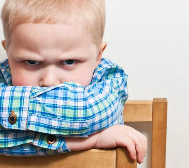 Bambino di 20 mesi ingestibile, con sguardo corrucciato e braccia incrociate sulla sedia.