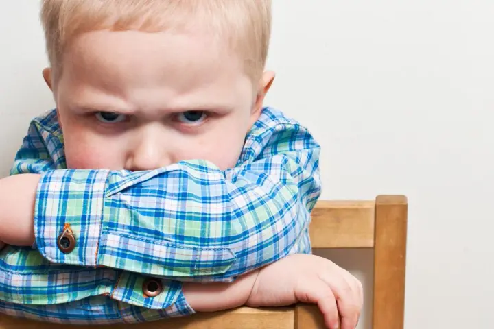 Bambino di 20 mesi ingestibile, con sguardo corrucciato e braccia incrociate sulla sedia.