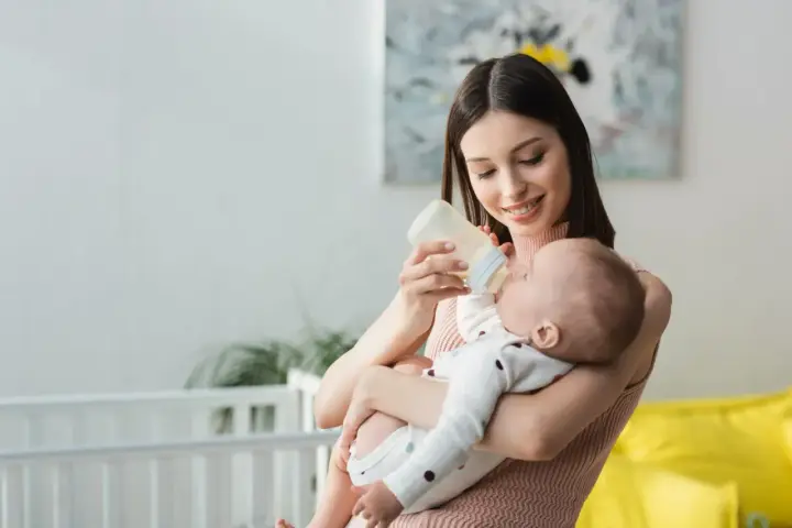 Mamma sorridente nutre il neonato con latte artificiale. Il piccolo potrebbe avere cacca liquida, ma ora è felice.