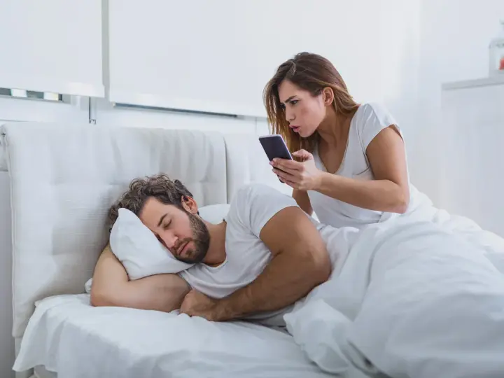 Donna guarda il telefono con sorpresa mentre il marito dorme. Sembra che mio marito abbia sempre il telefono in mano, anche a letto!