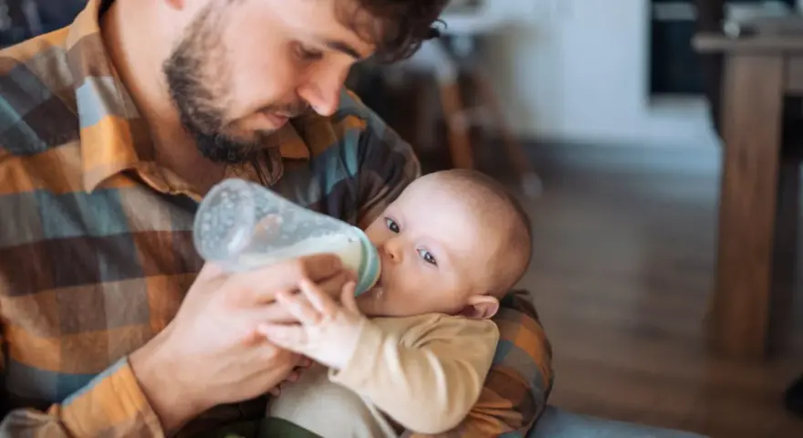 Padre con barba nutre il neonato con il biberon. Scopri trucchi per far prendere il biberon al tuo piccolo.