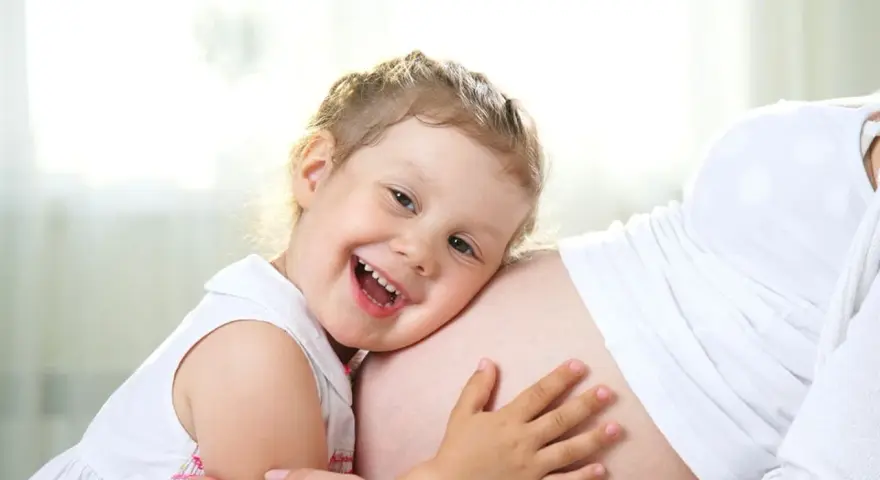 Bambina di 3 anni felice abbraccia la pancia della mamma, in attesa dell'arrivo di un fratellino.