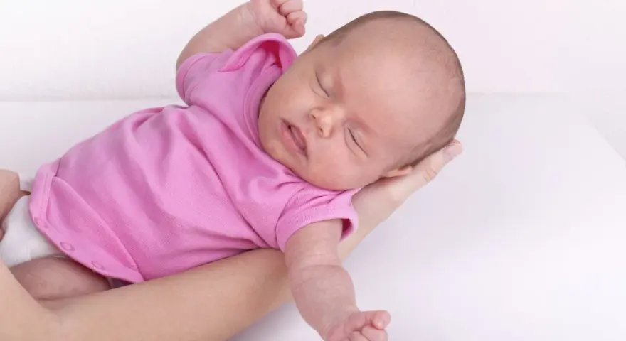 Neonato in rosa si irrigidisce e stringe i pugni, dormendo sereno tra le braccia.