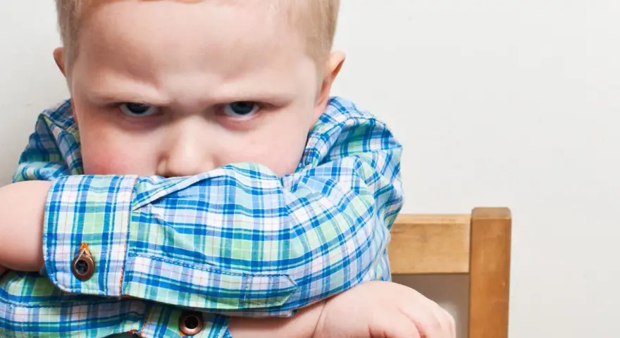 Bambino di 20 mesi ingestibile, con sguardo corrucciato e braccia incrociate sulla sedia.
