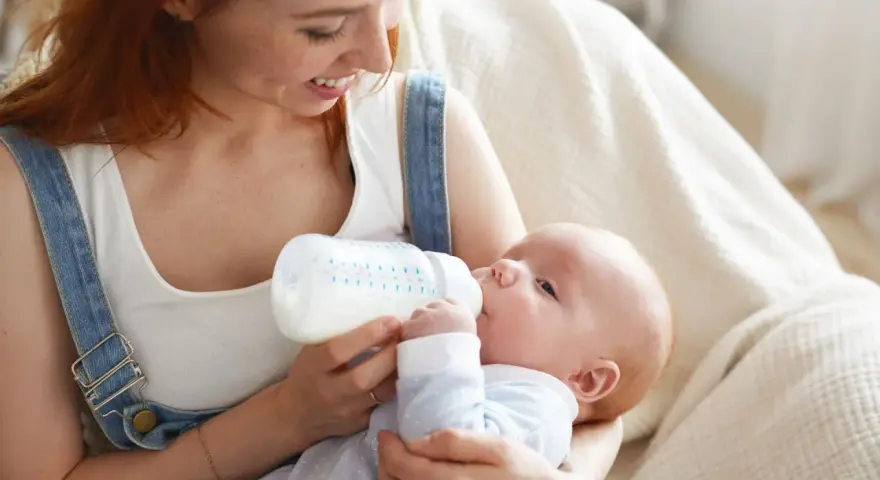 Mamma con capelli rossi nutre il suo neonato con latte artificiale ogni 2 ore. Il piccolo beve con gusto dalla bottiglia.