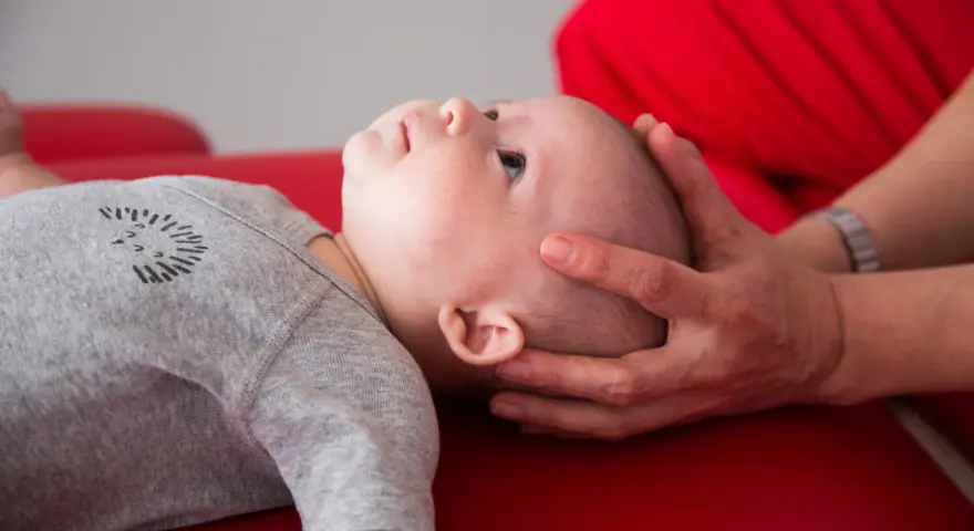Un neonato sbatte la testa sul petto, con mani adulte che lo sostengono delicatamente.