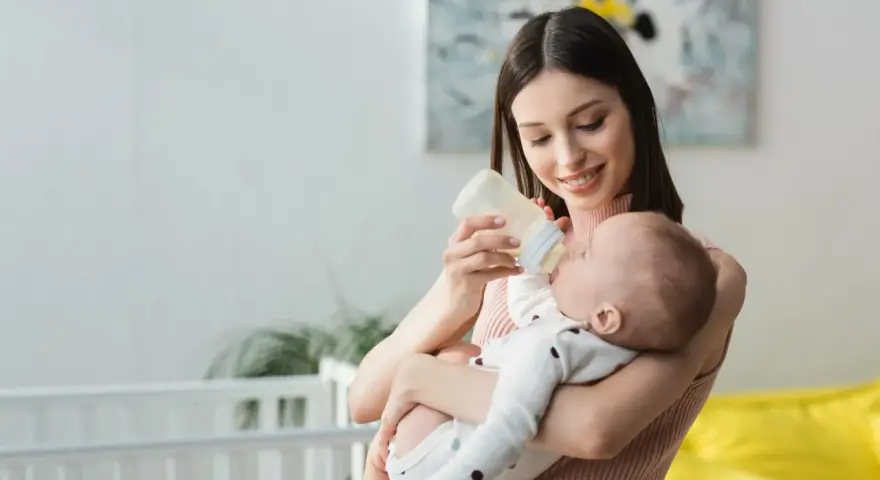 Mamma sorridente nutre il neonato con latte artificiale. Il piccolo potrebbe avere cacca liquida, ma ora è felice.