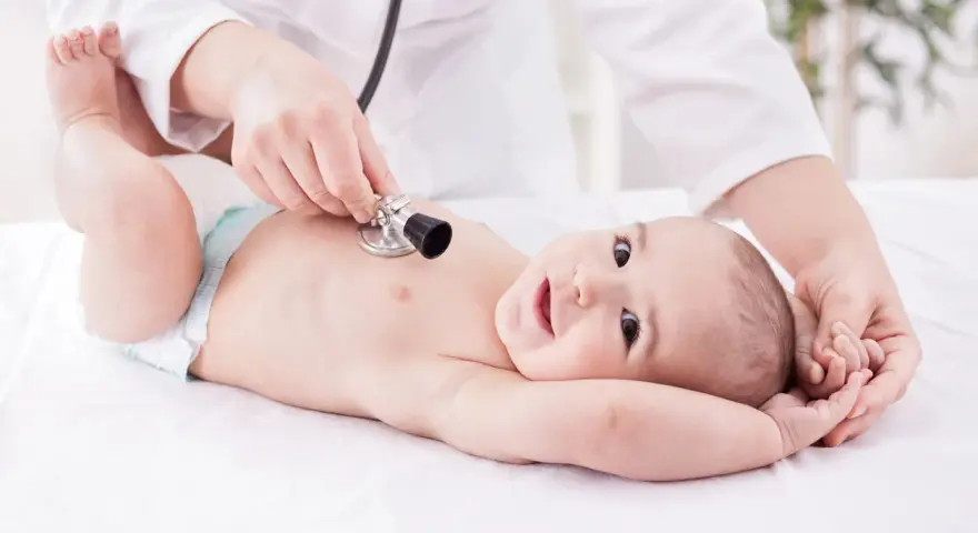 Un neonato sorride mentre il pediatra ascolta il suo respiro con uno stetoscopio.