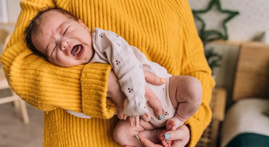 Neonato di 11 mesi con scatti nervosi, piange tra le braccia di chi lo tiene, avvolto in un maglione giallo.