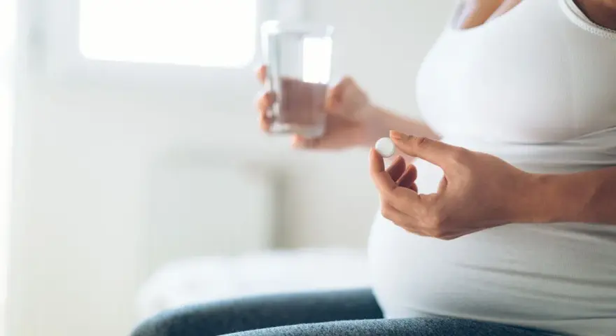 Donna incinta tiene una pillola e un bicchiere d'acqua. L'uso di cortisone in gravidanza va valutato attentamente.