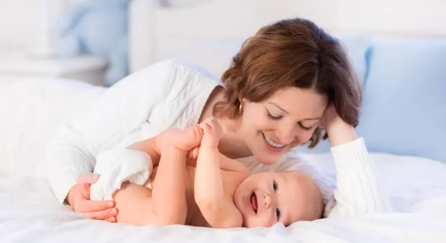 Mamma sorride mentre gioca con il suo neonato, svegliandolo dolcemente per mangiare.