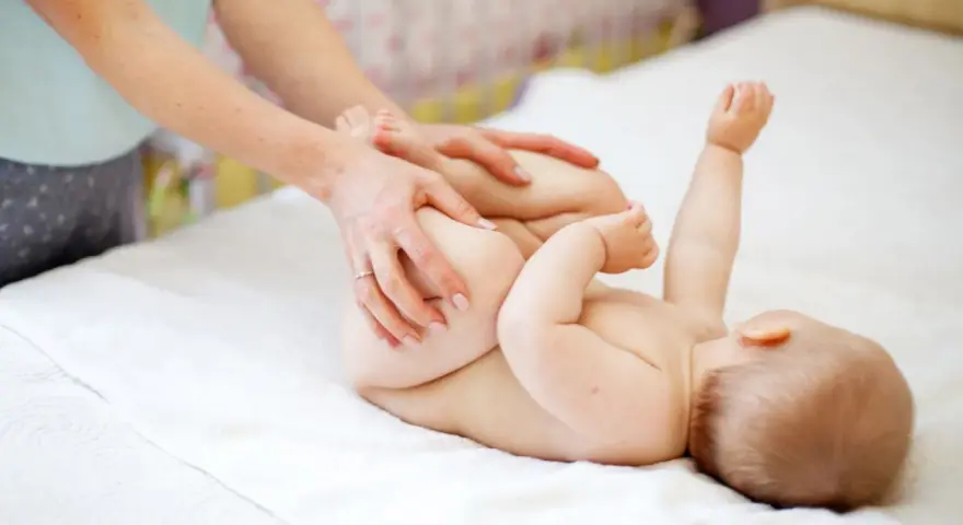 Mani che aiutano il neonato a fare la cacca con movimenti delicati sulle gambine.