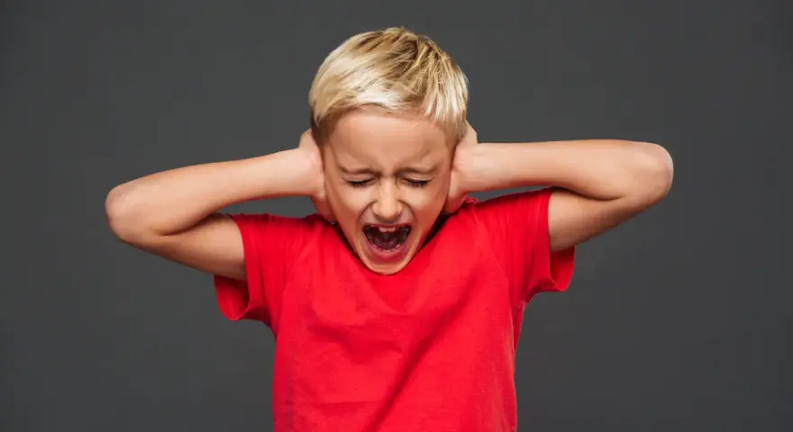 Bambino di 7 anni in crisi di rabbia, urla coprendosi le orecchie.