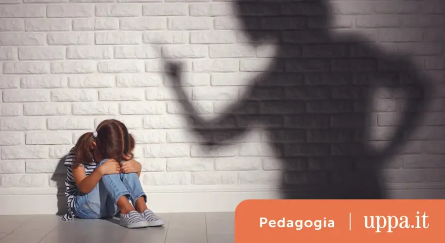 Bambina spaventata seduta a terra, ombra minacciosa di un adulto. Un'immagine che evoca le conseguenze delle punizioni corporali sui bambini.