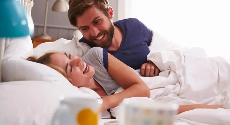 Coppia sorridente a letto, un momento di gioia che va oltre i rapporti promiscui, un legame profondo.