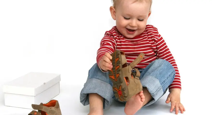 Bambino di 18 mesi, con un comportamento curioso, gioca con un sandalo marrone.