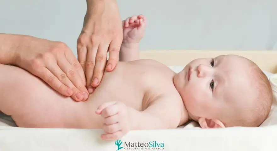 Mani che massaggiano la pancia di un neonato, forse per alleviare coliche o cacca acida. Un momento di cura per i più piccoli.