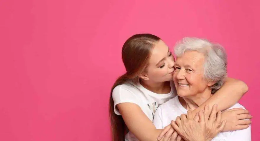 Una ragazza bacia la guancia della nonna, abbracciandola. Si vede che i figli assomigliano ai nonni, un legame d'amore.