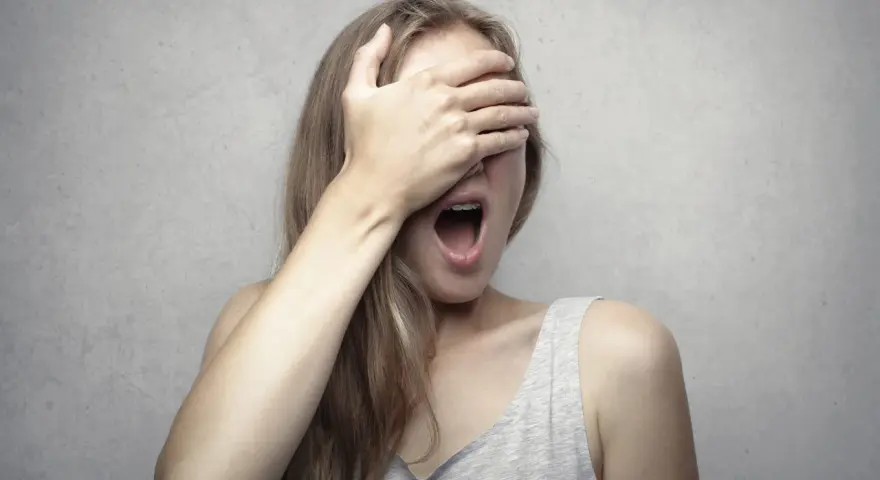 Ragazza con la mano sugli occhi, bocca spalancata, forse per la fobia del vomito (emetofobia).