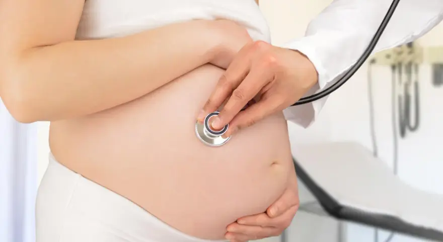 Visita medica per monitorare la gravidanza. Il medico ascolta il battito cardiaco del feto con uno stetoscopio sul pancione.