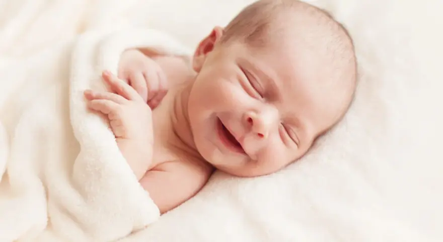 Un adorabile neonato non dorme, ma sorride beatamente avvolto in una coperta morbida.