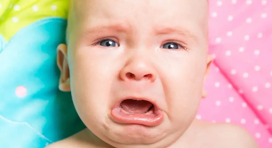 Un neonato piange dopo poppata, con gli occhi azzurri spalancati e la bocca aperta in un lamento.